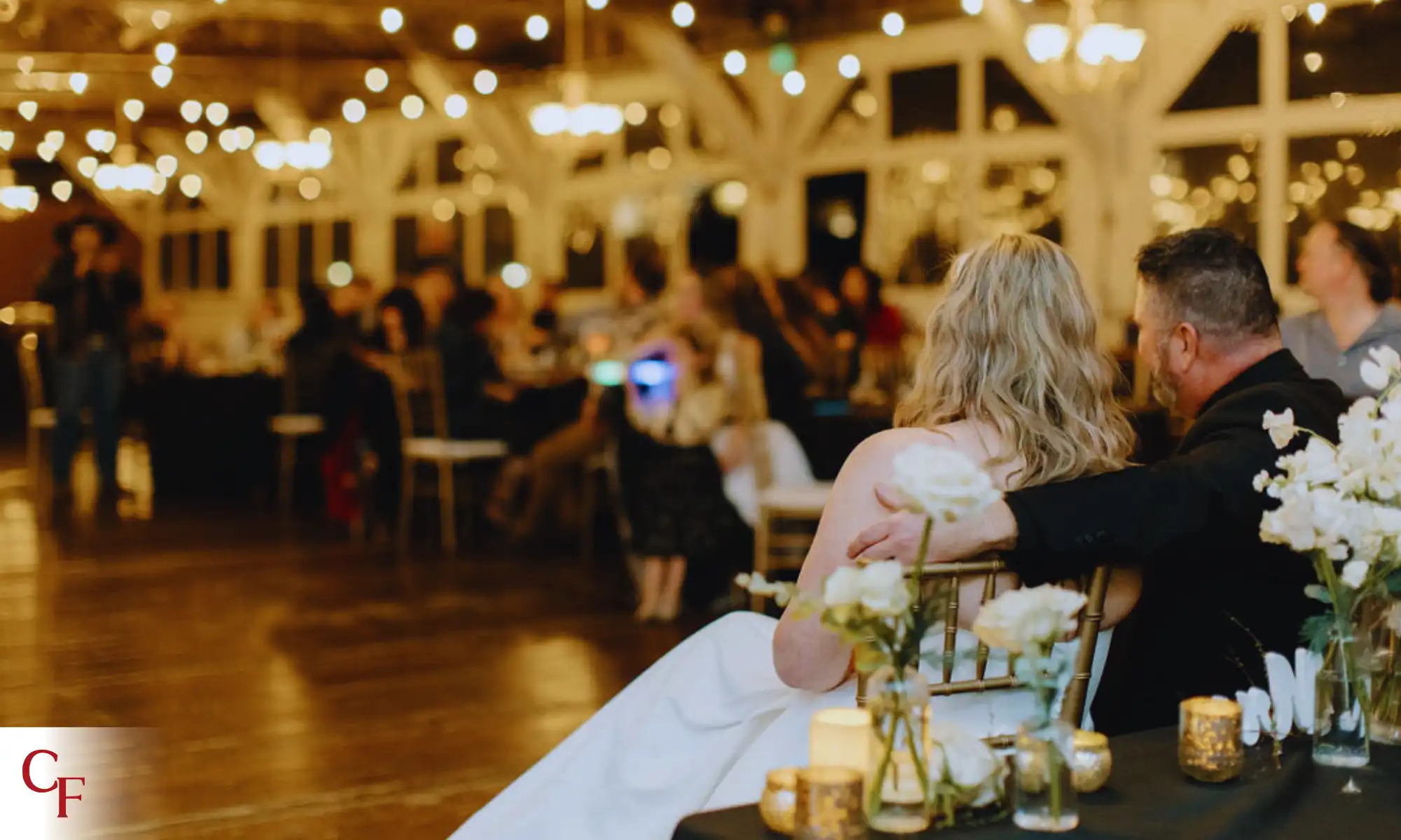 Bride and groom seated at rustic wedding reception with string lights at Carnation Farms
